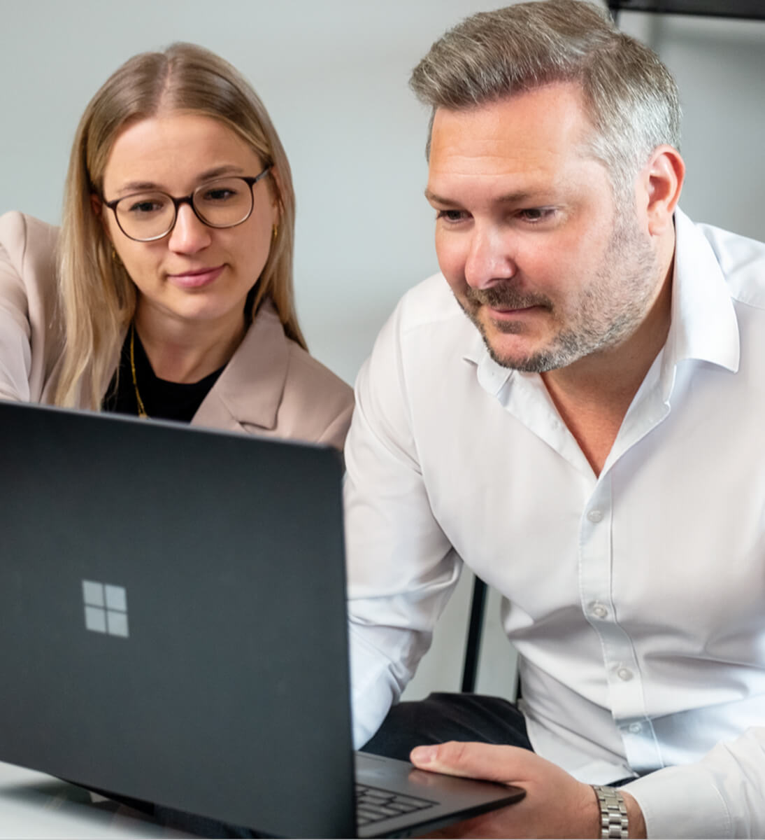 A man and a woman are sitting at the desk looking at something on the laptop screen in front of them. | google ads conversion audit SUNZINET