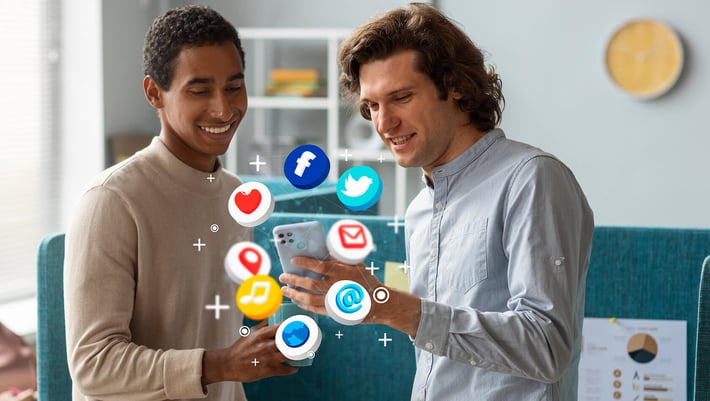 Zwei junge Männer schauen auf ein Smartphone, mittig im Bild und um das Smartphone herum im Kreis schweben Apps mit verschiedenen Symbolen der Online Kommunikation | B2B Marketing SUNZINET